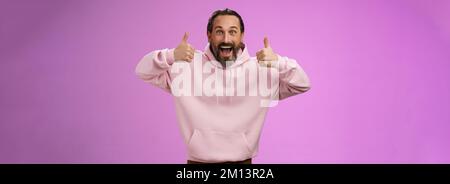 Eccitata energica, carismatica europea matura in rosa hoodie mostra pollici verso l'alto gesto sorridendo accordo di approvazione raccomandando Foto Stock