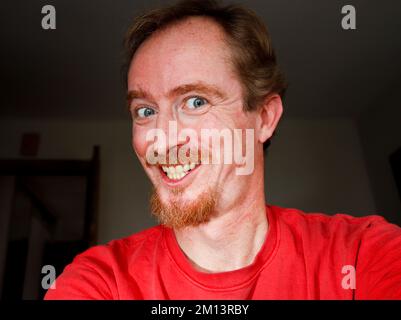 L'uomo dei capelli dello zenzero guarda dentro allo schermo del suo calcolatore o del tablet, leggendo qualcosa che cosa non è così divertente Foto Stock