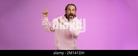 Impressionato scioccato scosso fresco hipster maturo 50s uomo sopportato grigio capelli in rosa felpa con cappuccio retelling incredibile storia puntando su indice le dita allargano gli occhi Foto Stock