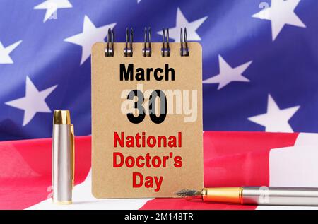 Vacanze USA. Sullo sfondo della bandiera degli Stati Uniti si trova un cartone con l'iscrizione - Giornata Nazionale dei Medici Foto Stock