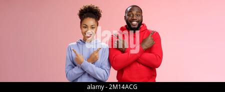 Affascinante coppia felice africano americano ragazzo ragazza muoversi insieme puntando diversi lati croce braccia petto sinistra destra sorridendo ampiamente Foto Stock