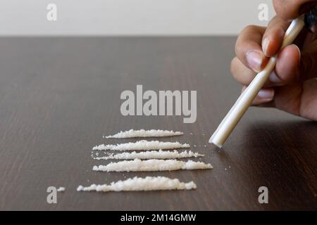 Immagine della mano del tossicodipendente che tiene carta avvolta insieme a righe di stupefacenti (cocaina ed eroina) Foto Stock