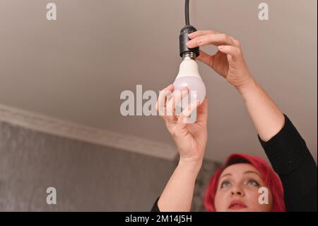 Una bella donna avvita una lampadina a LED nella cartuccia. Foto Stock