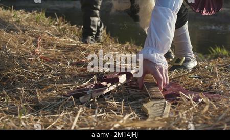 Uomo in vecchio costume e parrucca bianca che raccoglie la parte di chitarra rotta da erba secca, concetto storico spettacolo. Uomini in abiti antichi del 17 secolo prendendo GU Foto Stock