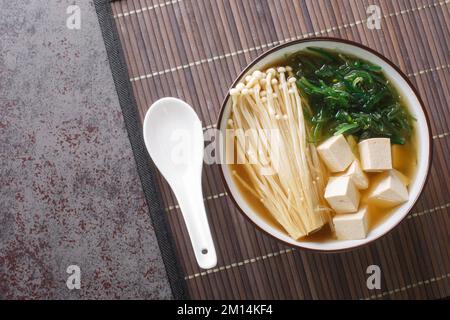 Zuppa di miso ricca con funghi enoki, alghe wakame e tofu, piatti vegetariani e vegani asiatici primo piano in una ciotola sul tavolo. Vista orizzontale dall'alto da A. Foto Stock