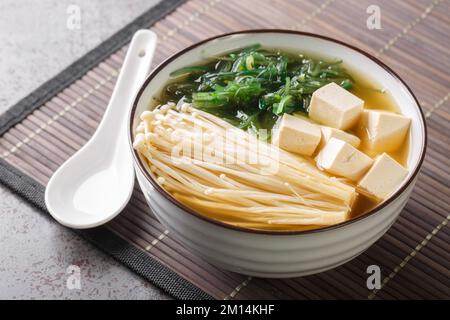 Zuppa di miso ricca con funghi enoki, alghe wakame e tofu, piatti vegetariani e vegani asiatici primo piano in una ciotola sul tavolo. Orizzontale Foto Stock