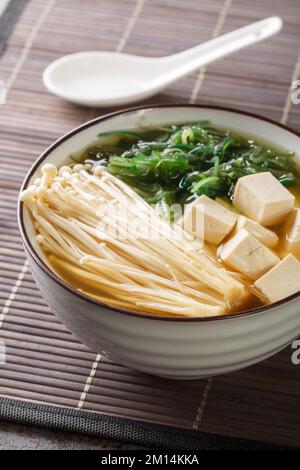 Zuppa di miso con tofu, funghi enoki, alghe wakame primo piano in una ciotola sul tavolo. Verticale Foto Stock