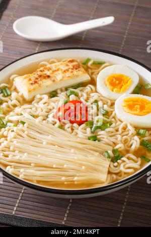 Zuppa asiatica di miso ramen con tagliatelle, uova, tofu e enoki in un recipiente sul tavolo. Verticale Foto Stock