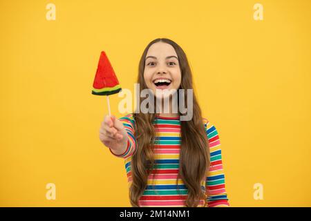 Bambino teen freddo con lollipop sopra sfondo isolato giallo. Dolce vita d'infanzia. Ragazza teen con caramella lollipop yummy. Foto Stock