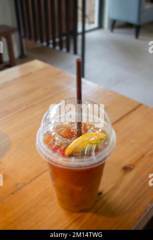 Tè al limone ghiacciato in tazza di plastica su tavolo di legno, foto di scorta Foto Stock