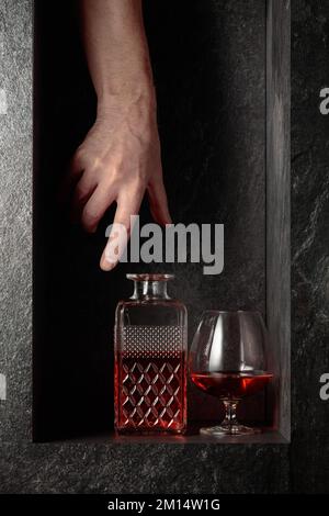 Sbraccio a mano per un decanter di brandy. Un'immagine concettuale sul tema delle bevande costose. Foto Stock