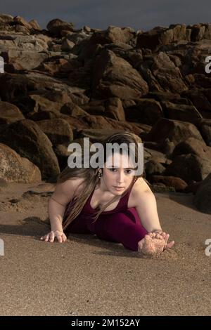 una giovane donna, che pratica yoga, fa un esercizio di stretching sulla spiaggia. donna divisa Foto Stock