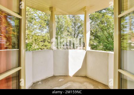 un balcone vuoto con alberi sullo sfondo e sole che splende attraverso le porte di vetro al secondo piano verso il patio Foto Stock