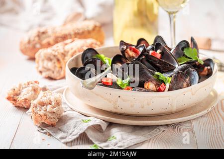 Cozze fresche e deliziose con peperoncino e coriandolo. Cozze in vino bianco e salsa all'aglio servite con pane. Foto Stock