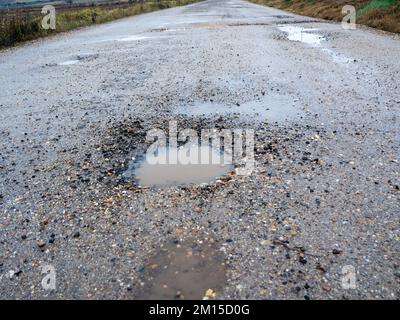 Pothole su una strada asfaltata in una giornata invernale piovosa. Concetto di rischio e problemi di traffico Foto Stock