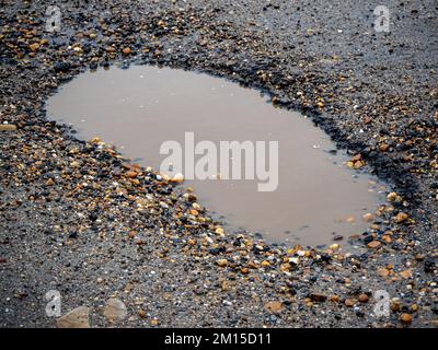 Pothole su una strada asfaltata in una giornata invernale piovosa. Concetto di rischio e problemi di traffico Foto Stock