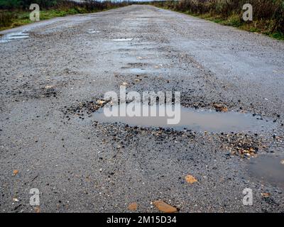 Pothole su una strada asfaltata in una giornata invernale piovosa. Concetto di rischio e problemi di traffico Foto Stock