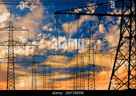 piloni ad alta tensione per l'elettricità e l'energia contro il cielo con nuvole drammatiche Foto Stock