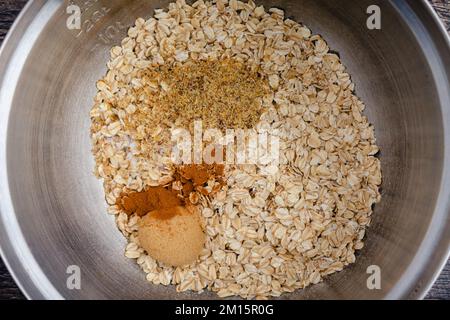 Ingredienti asciutti per la farina d'avena cotta in un Closeup della ciotola di miscelazione: Avena arrotolata, semi di lino macinati, cannella, zucchero di canna e sale in un recipiente grande Foto Stock