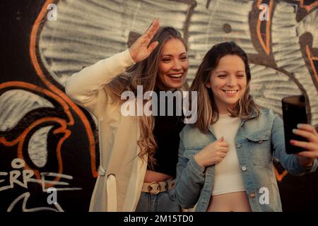 Due amiche sorridenti e scattano selfie contro un graffito Foto Stock