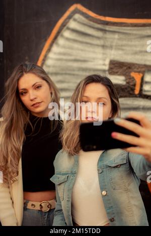 Immagine verticale di due amici femminili che scattano un selfie contro un graffito Foto Stock