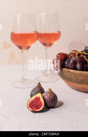 Bicchieri di bevanda rossa posti sul tavolo con ciotola di uva e fichi Foto Stock