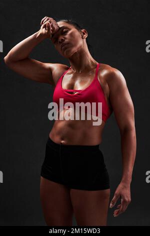 Donna in latino forte con top rosso e shorts con corpo perfetto in piedi su sfondo nero dopo l'allenamento Foto Stock