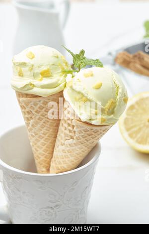 Un paio di gelato al limone fatto in casa in croccanti coni di waffle decorati con scorza e foglia di menta messi in tazza sul tavolo in cucina Foto Stock