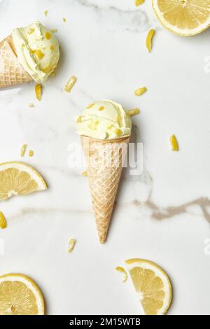 Vista dall'alto delle deliziose coppette di gelato in cialde disposte su un tavolo di marmo vicino alle fette e alla scorza di limone in cucina Foto Stock