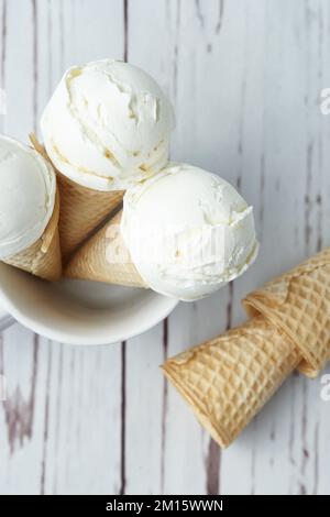 Vista dall'alto dei croccanti coni di waffle con palline di gelato alla vaniglia e mite poste in tazza su un tavolo di legno bianco durante il giorno Foto Stock