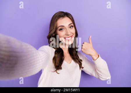 Primo piano selfie cadre di giovane adorabile bella blogger donna indossare bianco pullover pollice up raccomandare annuncio isolato su sfondo di colore viola Foto Stock