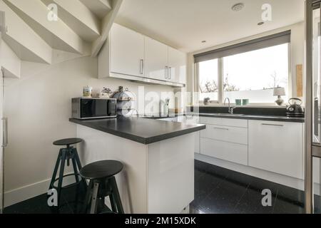 Banconi bianchi con lavello e elettrodomestici posizionati contro la parete con mobili incorporati in cucina leggera a casa Foto Stock