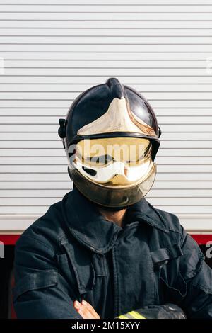 Irriconoscibile auto assicurato anonimo pompiere maschio in uniforme protettiva e casco incrociando le braccia mentre si trova contro la porta del garage Foto Stock