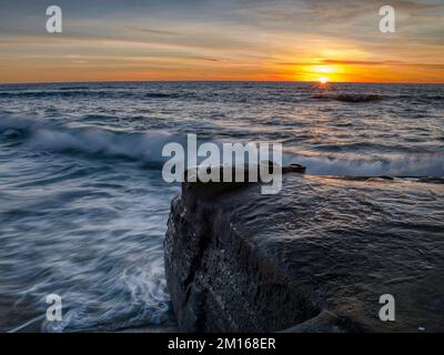 Uno scatto panoramico di una collina rocciosa nel mare ondulato al tramonto Foto Stock