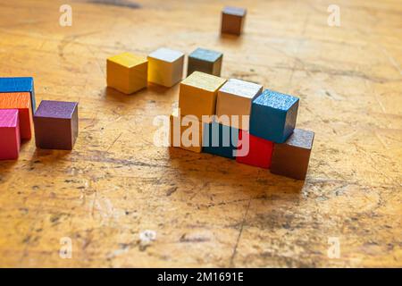 Una fila di piccoli cubetti di legno colorati, parzialmente impilati, su una vecchia superficie di legno usurata Foto Stock