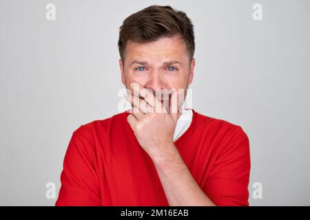 uomo piangente e sconvolto in un maglione rosso. Non essere timido a piangere concetto. Foto Stock