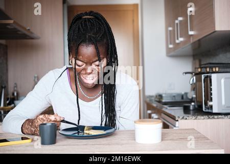 Allegra donna nera che fa colazione in cucina Foto Stock