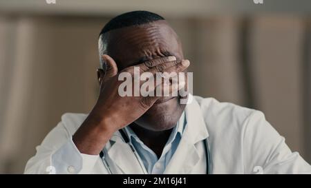 Uomo africano stanco medico medico professionista medico strofinare irritato occhi massaggiando faccia maschio terapista etnico esausto dopo il giorno di lavoro Foto Stock
