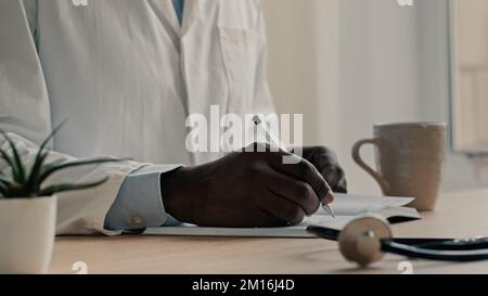 Uomo irriconoscibile medico terapeuta cardiologo indossa il cappotto medico sedersi alla scrivania scrivere diagnosi in notebook pianificazione giorno di lavoro prescrivere medicina Foto Stock