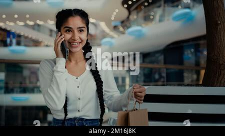 Ragazza araba femmina acquirente cliente acquirente donna shopaholic parlare telefono al centro commerciale controllare acquisti borse regalo da lussuoso negozio di stoffa parlare Foto Stock