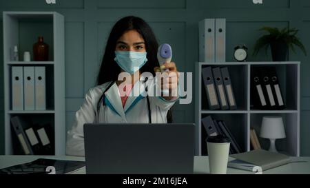 Giovane donna medico infermiera in maschera di protezione misurazione della temperatura con termometro a infrarossi senza contatto controllo digitale scanner elettronico Foto Stock