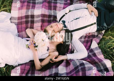 Splendida sposa e elegante sposo sdraiato su una plaid viola. Cerimonia nuziale di lusso in giardino. Primo piano. vista dall'alto. Foto Stock