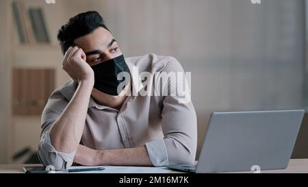 Annoiati triste ispanico lavoratore giovane uomo d'affari in maschera medica stanco dipendente non motivato disinteressato a lavoro torto lontano su computer pigro maschio arabo Foto Stock