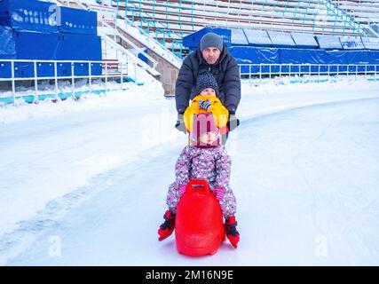 la famiglia corre sulla pista di pattinaggio. assistenza per imparare a pattinare. animale pattinaggio su ghiaccio Foto Stock