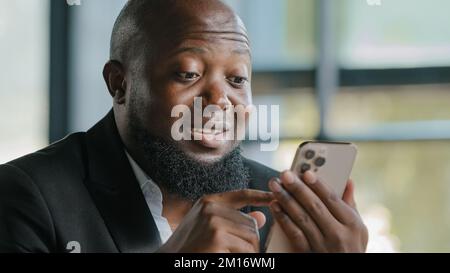 Felice uomo d'affari afroamericano alto bello bearded adulto uomo insegnante allenatore dipendente leggere buone notizie sul sito web chattando l'uso di app mobile Foto Stock