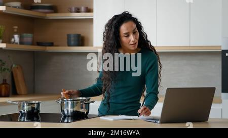 Donna araba madre cucina pranzo pranzo pasto cibo sano in cucina moderna scrivere ricetta internet utilizzando utile sito web di cucina sul laptop menu di un libro di cucina Foto Stock