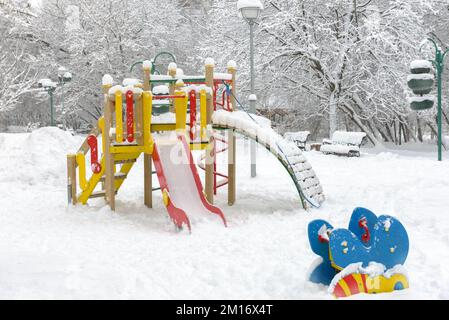 Parco giochi in inverno, Mosca, Russia. Parco deserto durante le nevicate, vista panoramica del parco giochi vuoto sotto la neve. Tema del tempo vinoso, della natura, della neve Foto Stock