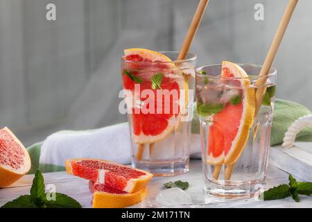Cocktail estivi rinfrescanti con fette di pompelmo e menta su un vassoio di legno bianco Foto Stock