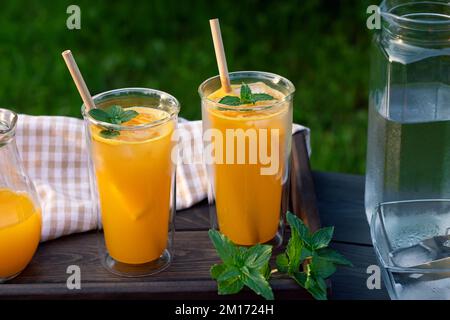 Rinfrescante cocktail estivo all'arancia fatto in casa in alti bicchieri doppi di vetro con menta e ghiaccio, focus selettivo. Foto Stock