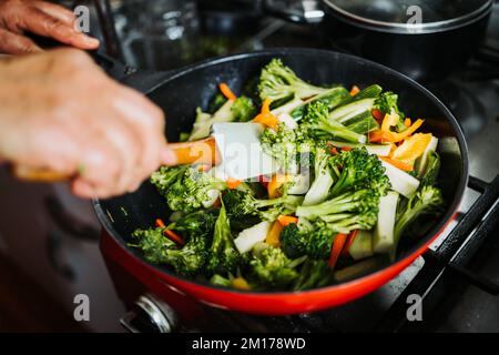 Primo piano delle mani di una donna latina che friggerà e mescolerà le verdure su una padella. Cibo vegetariano Foto Stock